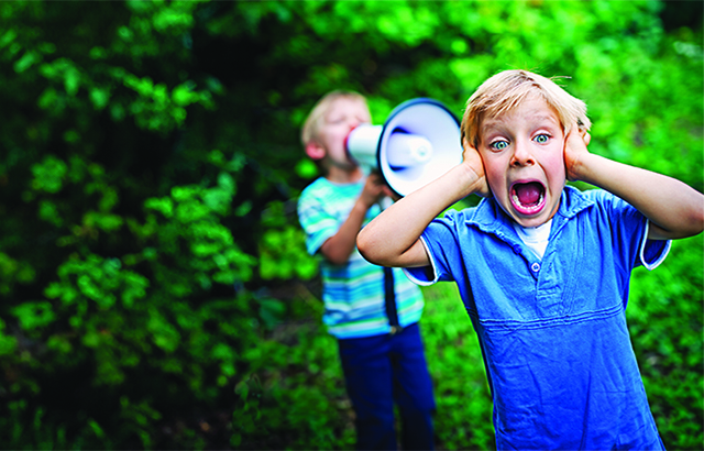 Little boy covering his ears while his brother is yelling on him with megaphone.